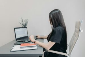 Person seated at a desk adjusts a monitor while keeping the head aligned over the shoulders.